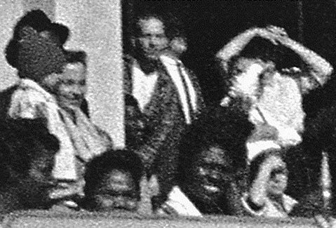 The Oswald Innocence Campaign says this photograph shows Lee Harvey Oswald (in the middle of the image, looking toward the camera) in the doorway of the book depository when JFK was shot